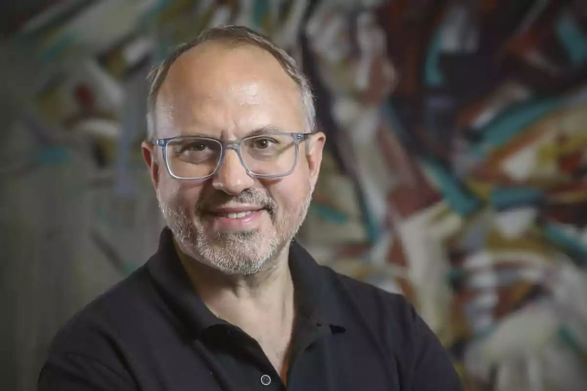 Middle-aged man with glasses and a beard smiles in front of a colorful, abstract background. Middle-aged man with glasses and a beard smiles in front of a colorful, abstract background.