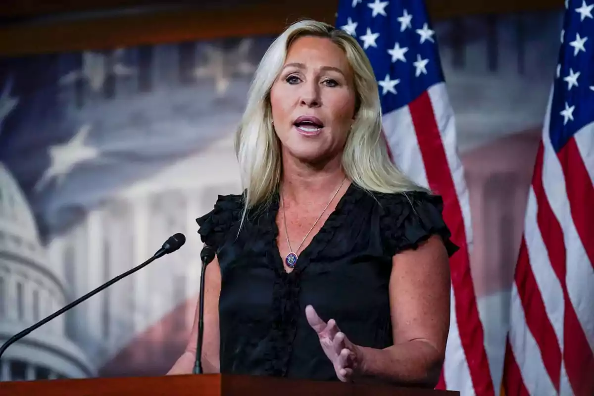 A blonde-haired woman speaks at a podium with American flags in the background.