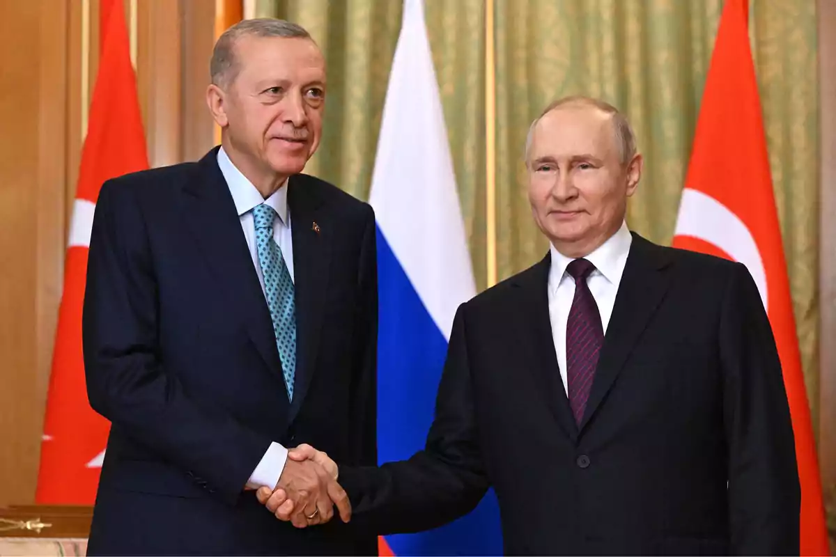 Dos hombres de traje oscuro se dan la mano frente a banderas de Turquía y Rusia. Dos hombres de traje oscuro se dan la mano frente a banderas de Turquía y Rusia.