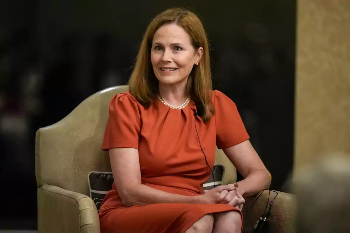 A woman in a red dress is sitting on a chair, smiling and looking forward.