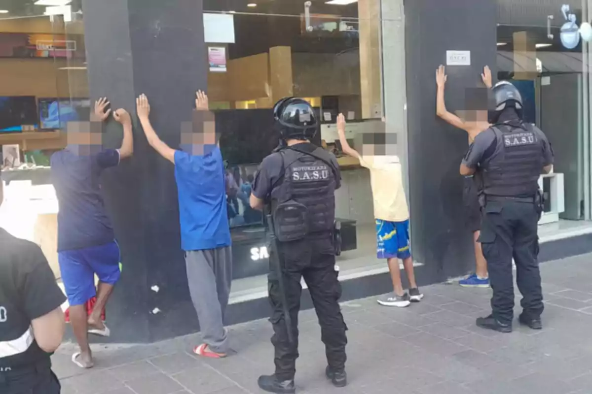 Un grupo de personas está siendo revisado por agentes de policía frente a un establecimiento comercial.