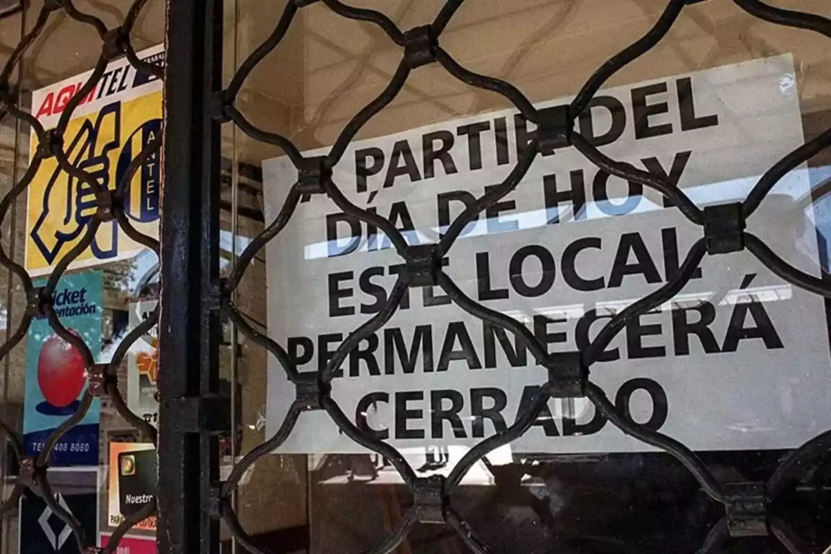 Sign on the door of a business announcing its permanent closure, seen through a metal gate