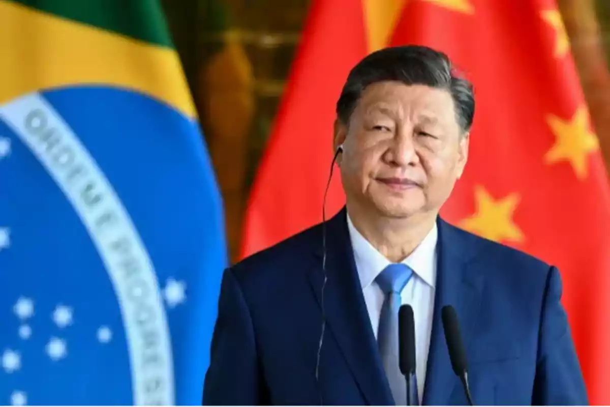Un hombre en traje oscuro con corbata azul está frente a dos banderas, una de Brasil y otra de China.