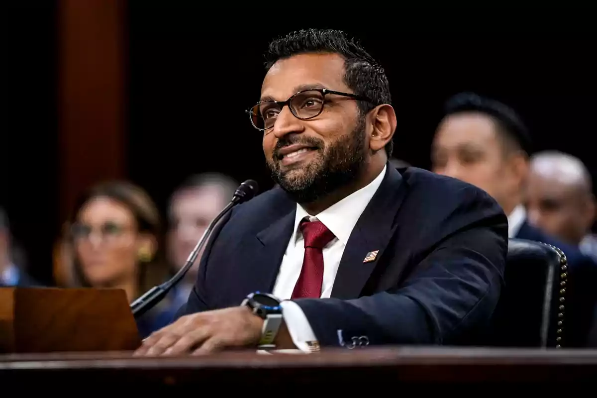 Hombre con barba y gafas usando traje oscuro y corbata roja hablando frente a un micrófono en una audiencia pública Hombre con barba y gafas usando traje oscuro y corbata roja hablando frente a un micrófono en una audiencia pública