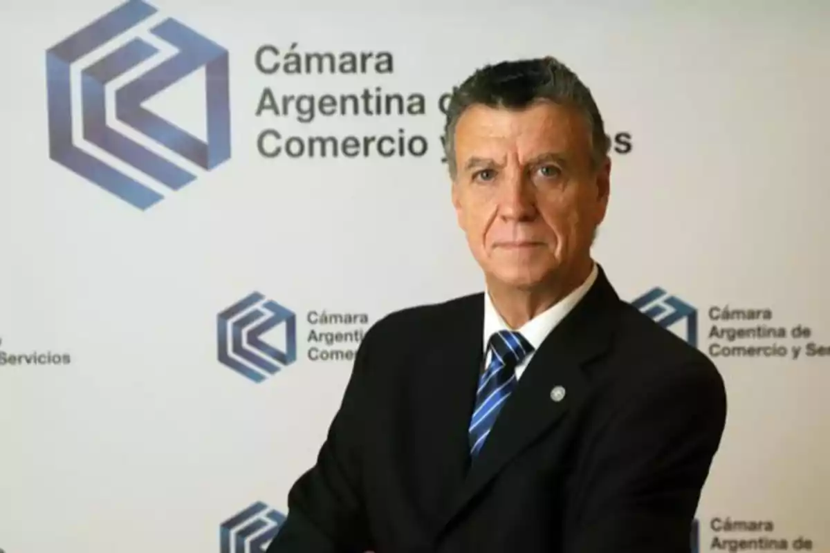 Hombre de traje frente a un fondo con el logo de la Cámara Argentina de Comercio y Servicios.