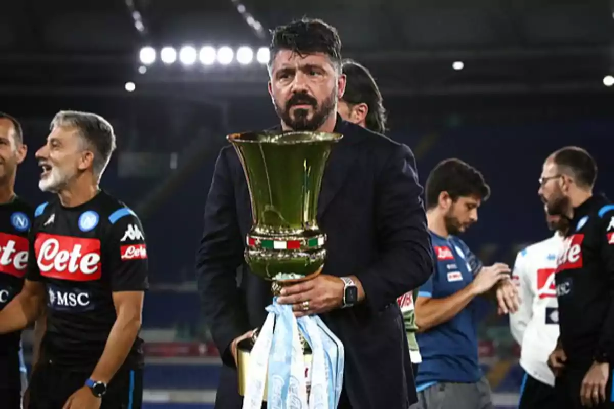 Napoli coach holding a large trophy while the team celebrates in the background Napoli coach holding a large trophy while the team celebrates in the background