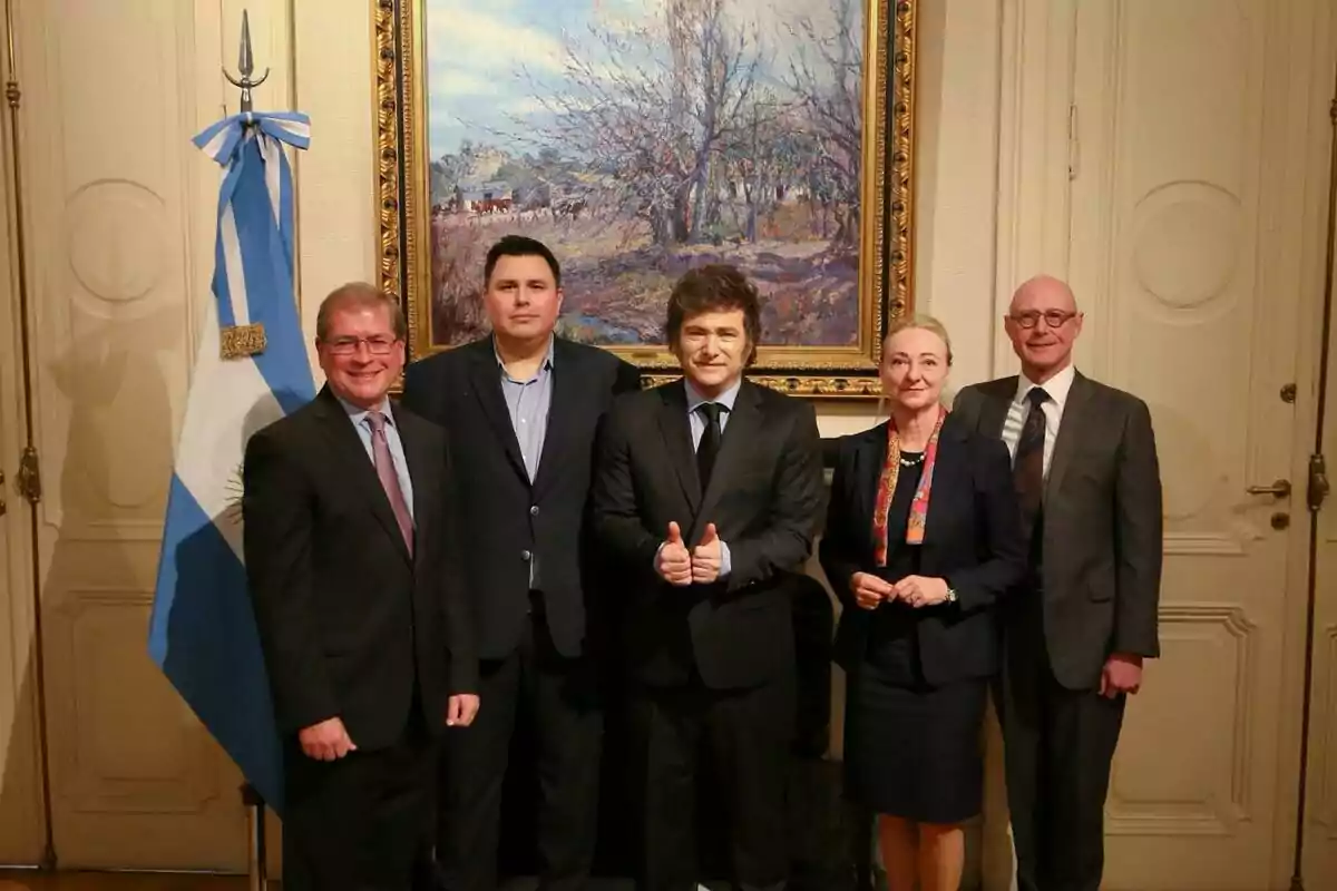 Un grupo de personas posando frente a una bandera argentina y un cuadro en una sala elegante.