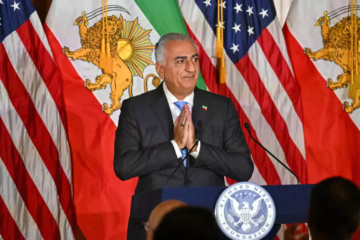Hombre de cabello canoso con traje oscuro y corbata azul hablando en un podio con el logo de la Fundación Richard Nixon, rodeado de banderas de Estados Unidos y banderas con un león dorado Hombre de cabello canoso con traje oscuro y corbata azul hablando en un podio con el logo de la Fundación Richard Nixon, rodeado de banderas de Estados Unidos y banderas con un león dorado