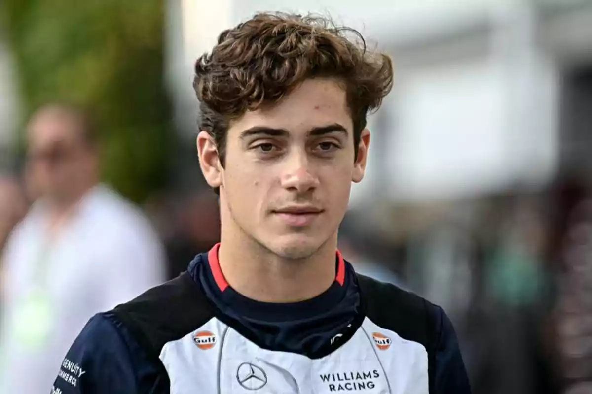 Un joven con cabello rizado lleva un uniforme de carreras con logotipos de patrocinadores.