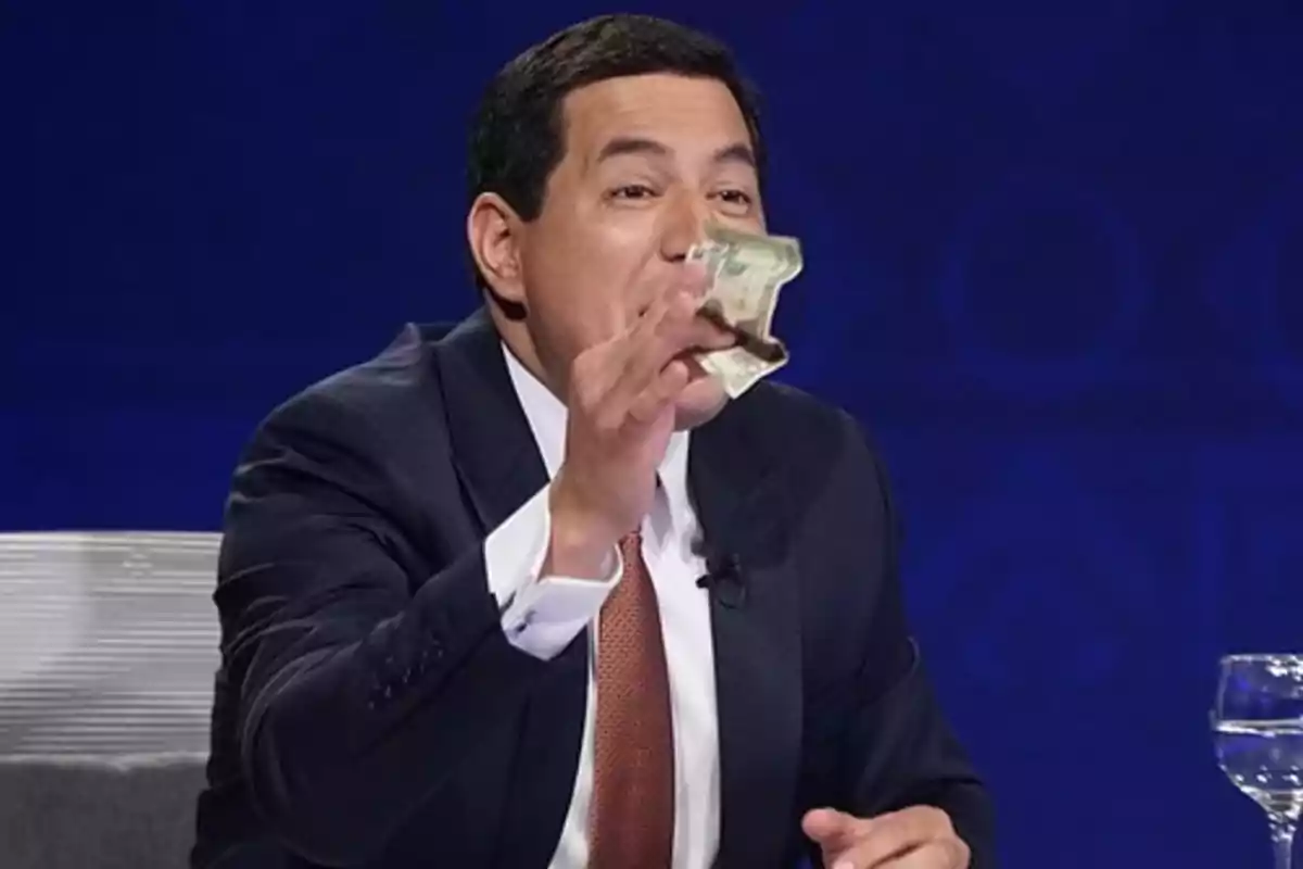 Hombre en traje sosteniendo un billete en un entorno de debate o entrevista.