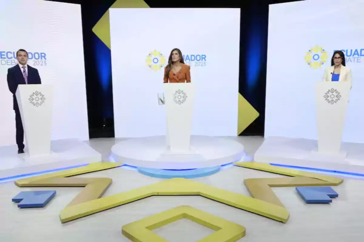 Three people standing behind podiums on a stage with the logo of a debate in Ecuador 2023.