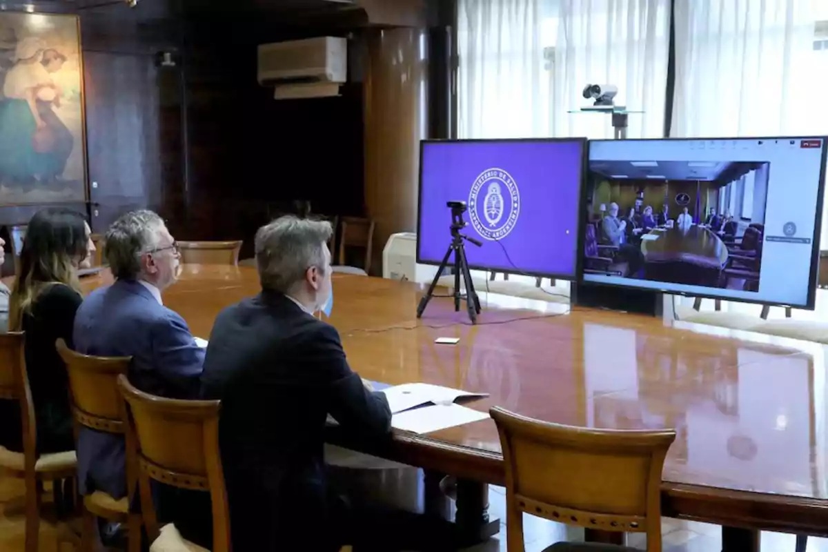 People in a conference room participating in a video call with a large screen showing other participants. People in a conference room participating in a video call with a large screen showing other participants.