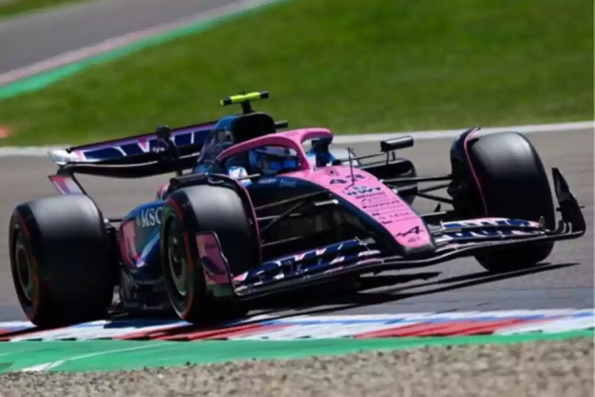A Formula 1 race car with a pink and blue design on a track during a competition. A Formula 1 race car with a pink and blue design on a track during a competition.