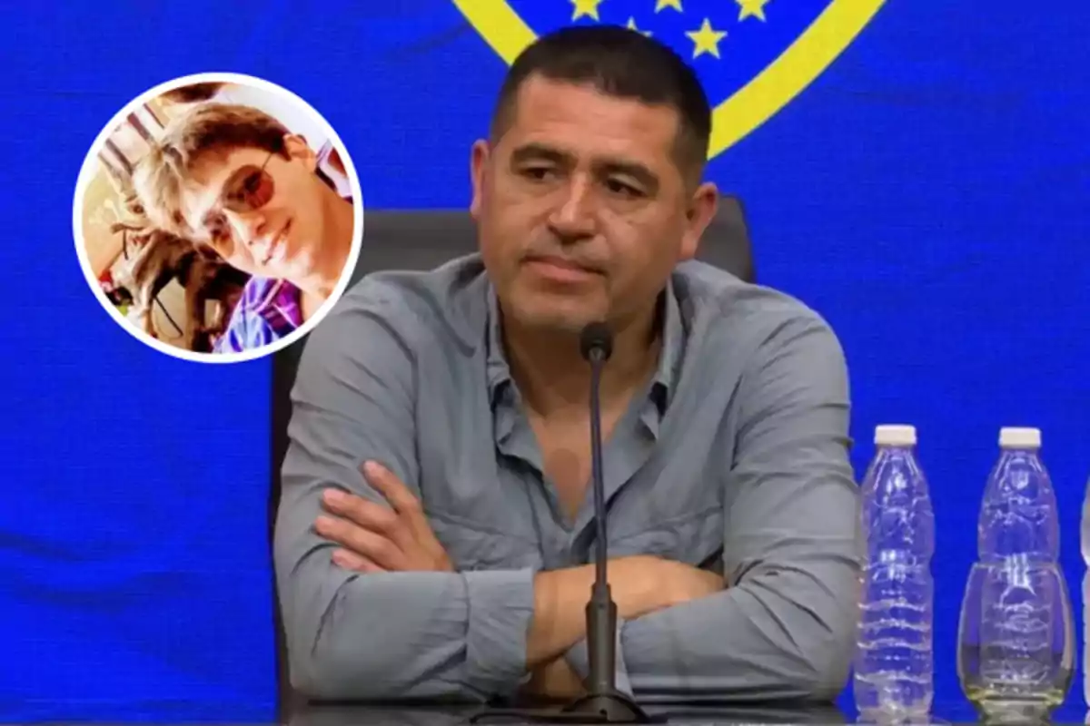 A man in a gray jersey is sitting in front of a microphone with his arms crossed, there are water bottles next to him and a blue background with a yellow shield, in the top left corner there is a circular frame with the image of another person wearing sunglasses.