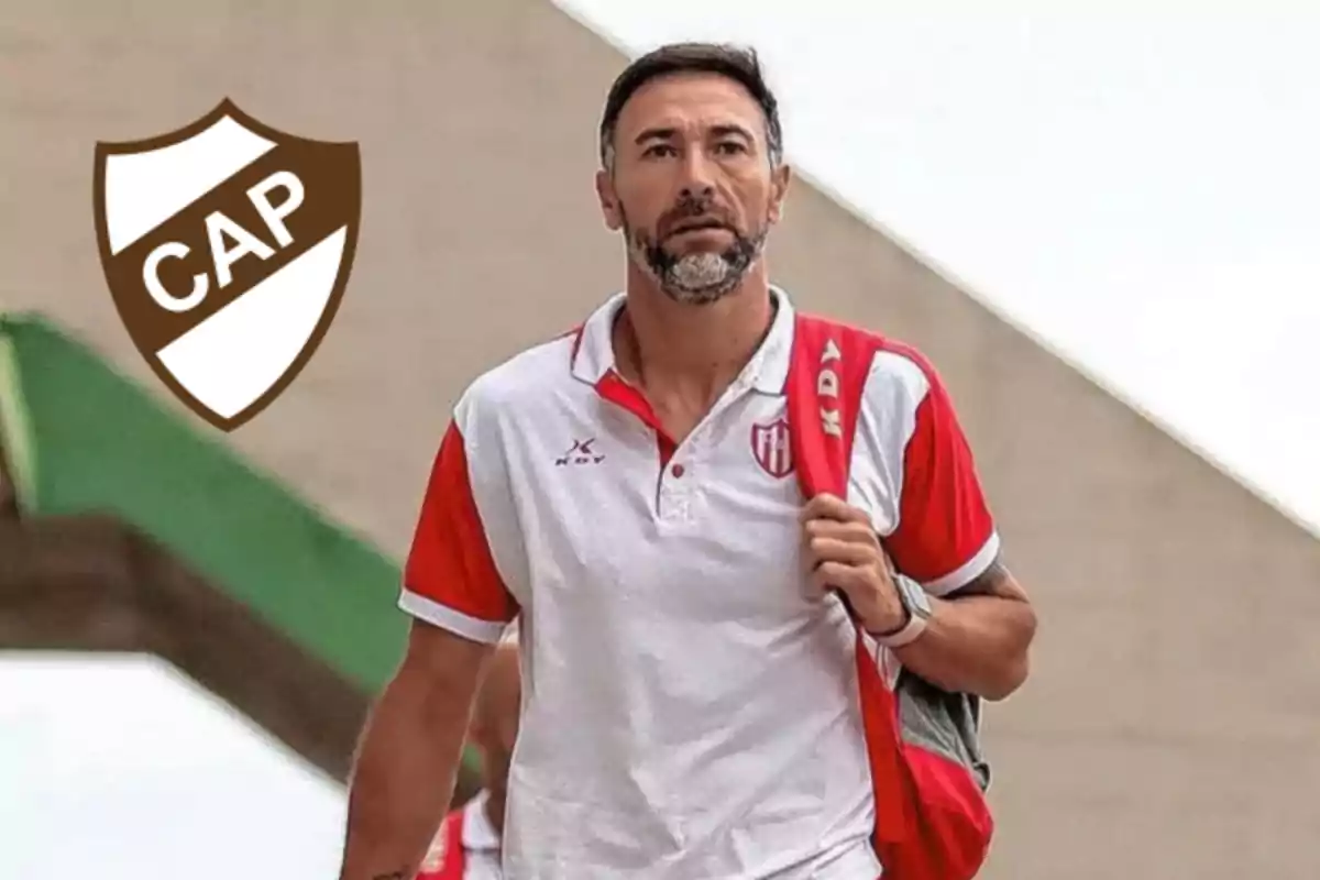 Hombre con barba y camiseta deportiva blanca con rojo caminando con una mochila roja y un escudo marrón con las letras CAP a la izquierda