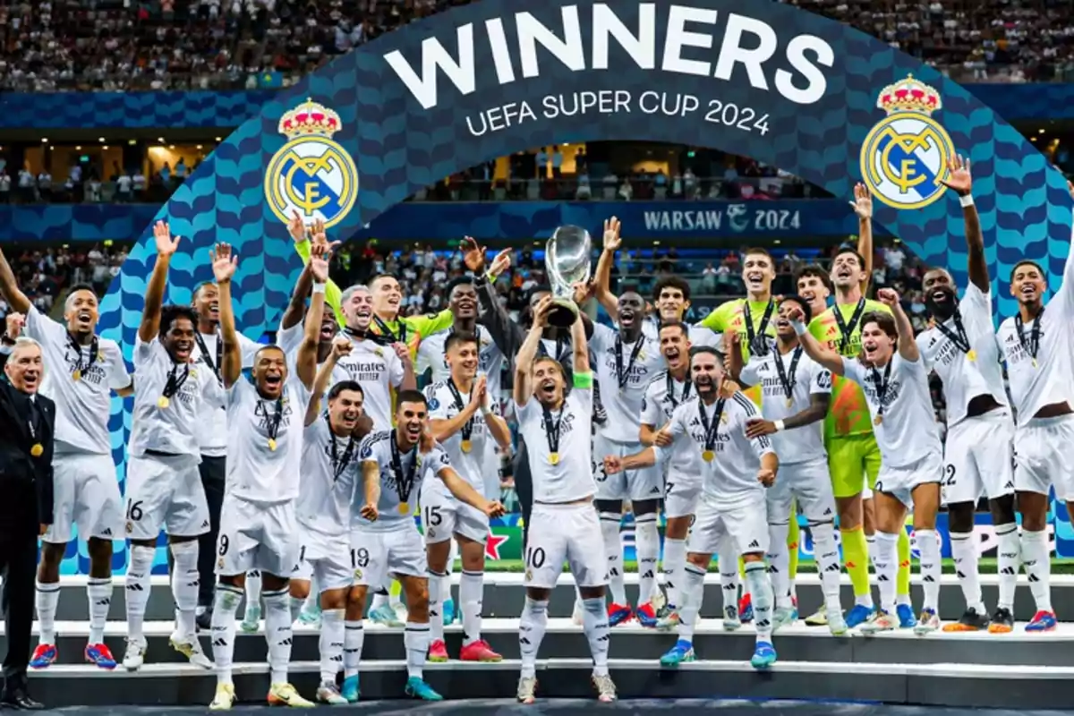 Jugadores de un equipo de fútbol celebran con un trofeo en un estadio bajo un cartel que dice "Winners UEFA Super Cup 2024".