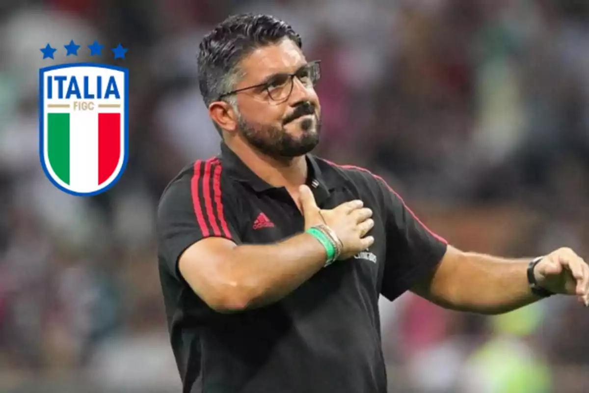 Man with glasses and a beard wearing a black jersey with red details, making a gesture with his hand on his chest and the Italy national football team crest on the left.