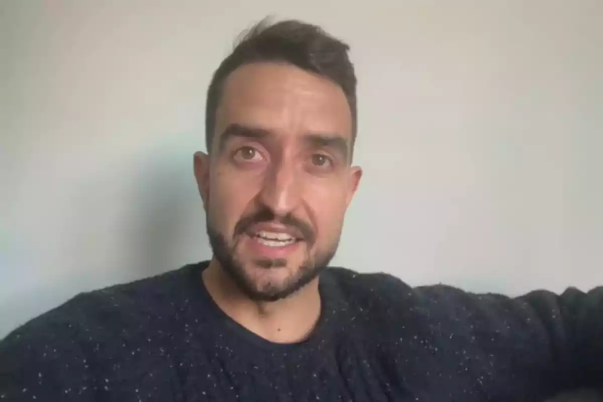 Un hombre con barba y cabello corto está hablando frente a una pared blanca. Un hombre con barba y cabello corto está hablando frente a una pared blanca.