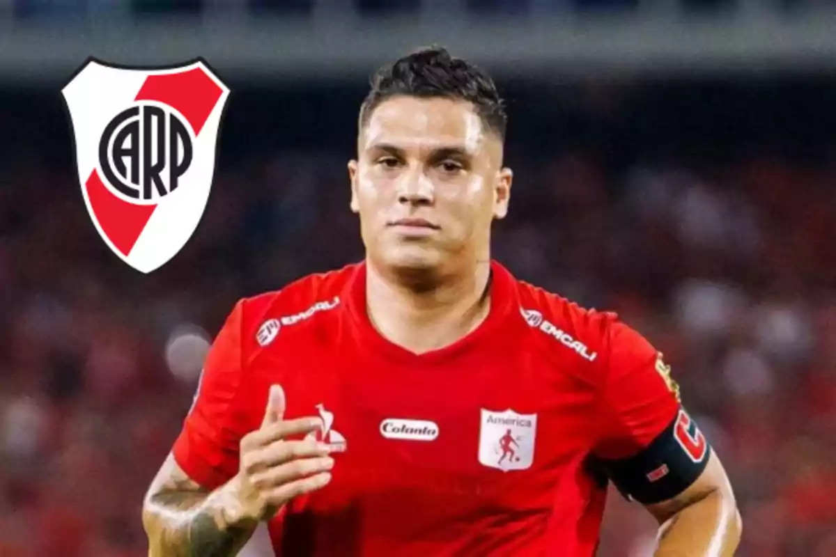 Soccer player wearing a red América de Cali jersey with a River Plate crest in the background