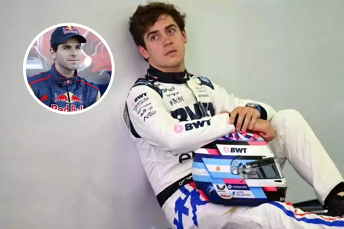 Motorsport driver in a white suit with a helmet resting on their legs, sitting next to a wall with a frame showing another driver in a blue uniform and cap.