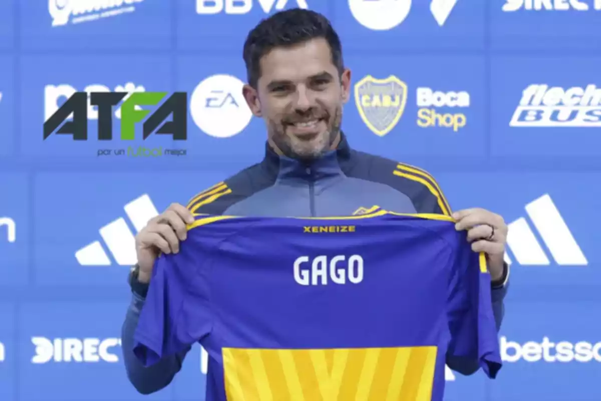 Un hombre sonriente sostiene una camiseta de fútbol azul y amarilla con el nombre Un hombre sonriente sostiene una camiseta de fútbol azul y amarilla con el nombre