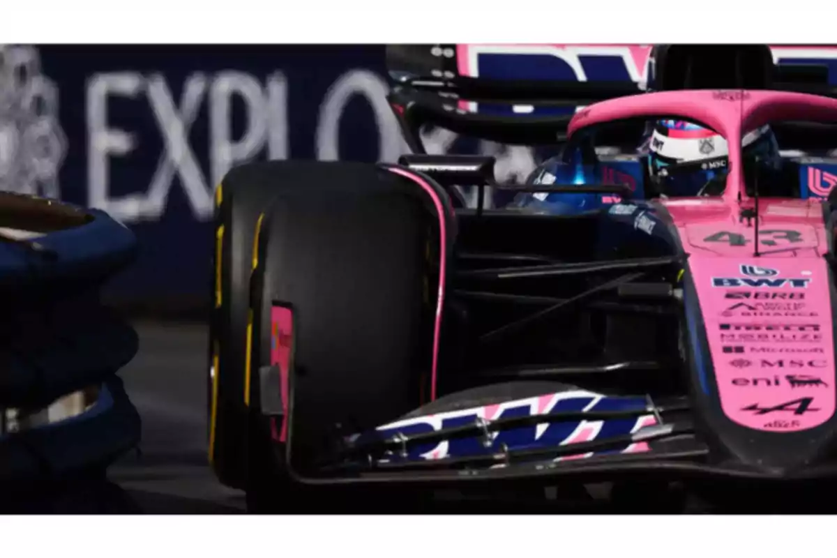 A pink and blue Formula 1 race car on a track, with a visible front tire and a blurred background. A pink and blue Formula 1 race car on a track, with a visible front tire and a blurred background.