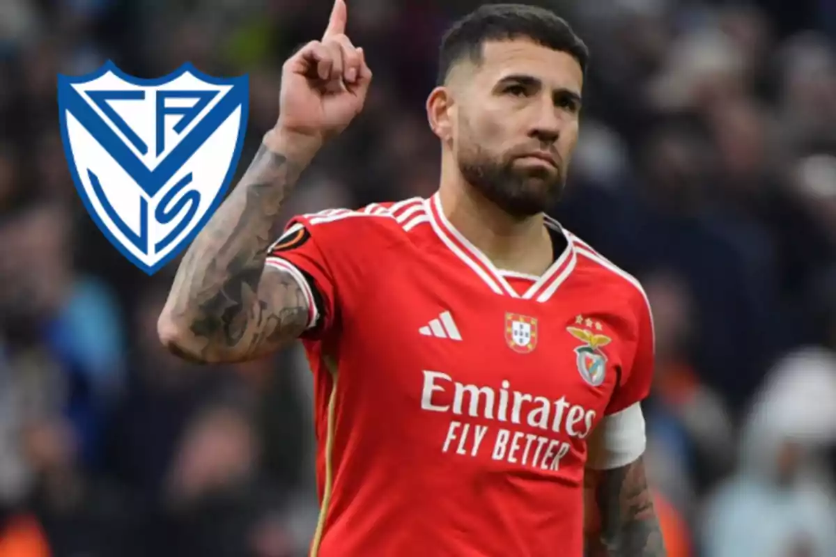 Soccer player in a red Benfica uniform raising one finger with the Vélez Sarsfield crest in the background