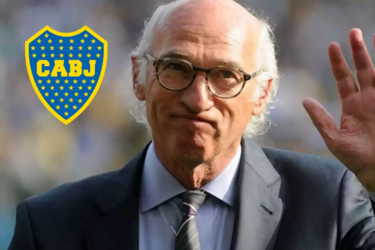 Un hombre mayor con gafas y traje saluda con la mano levantada, junto a un escudo del club de fútbol Boca Juniors.
