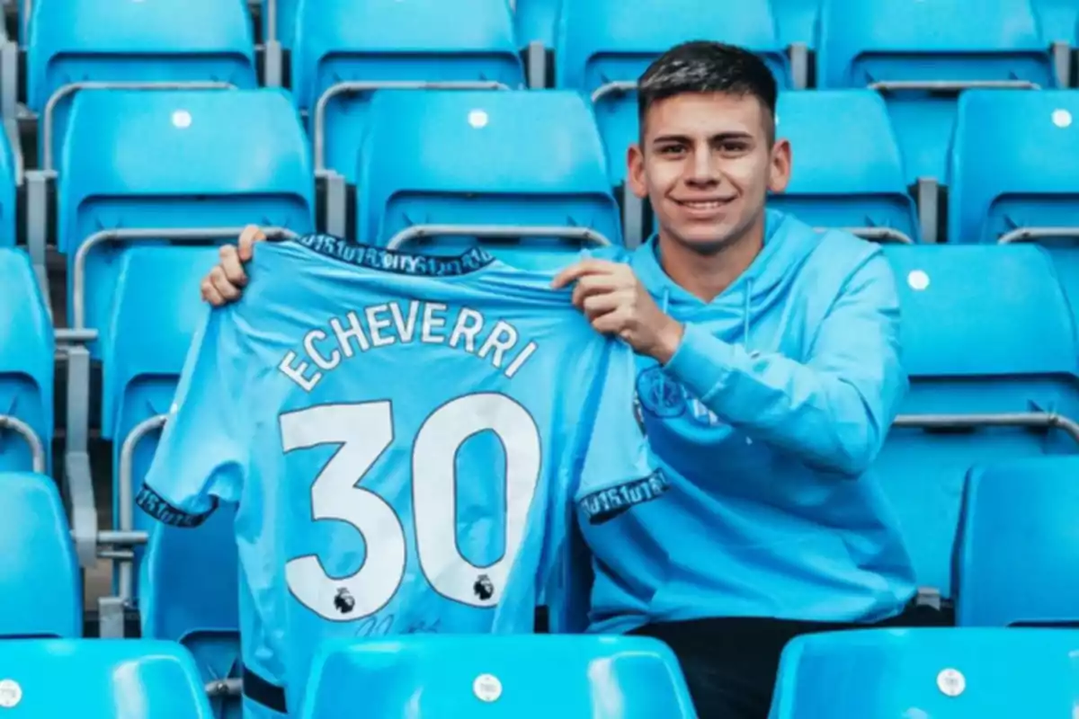 A young man sitting in the bleachers of a stadium holds a blue soccer jersey with the name A young man sitting in the bleachers of a stadium holds a blue soccer jersey with the name