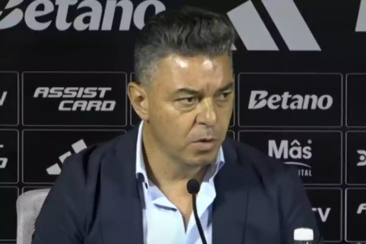 Un hombre en una conferencia de prensa con un fondo de logotipos de patrocinadores.