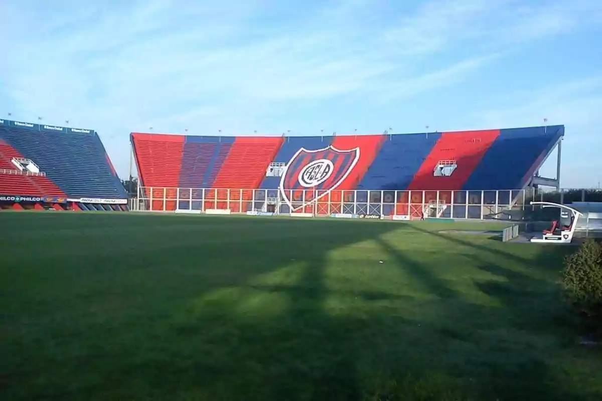 Tribuna de estadio de fútbol con asientos rojos y azules y un gran escudo de San Lorenzo en el centro Tribuna de estadio de fútbol con asientos rojos y azules y un gran escudo de San Lorenzo en el centro