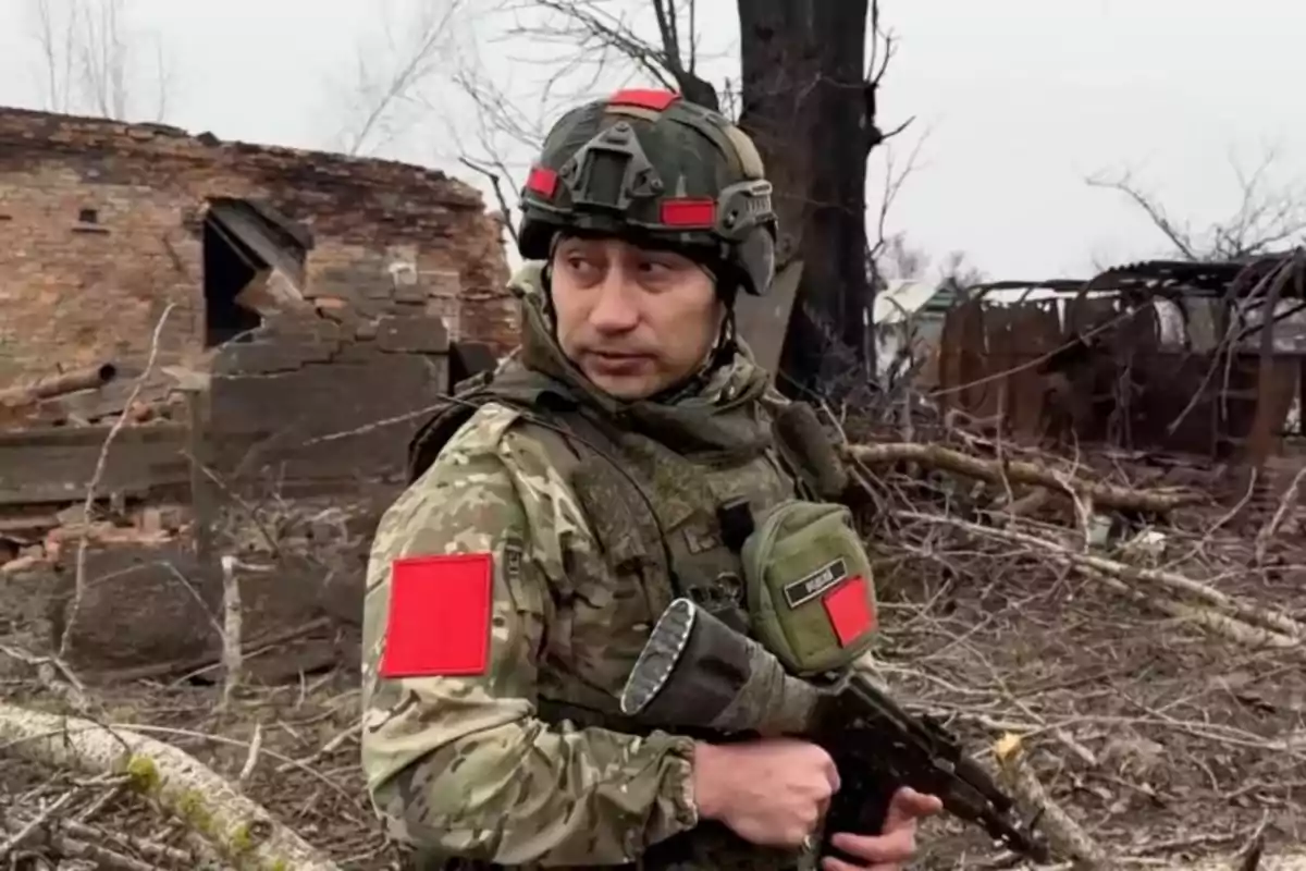 Un soldado con uniforme de camuflaje y casco sostiene un arma en un entorno de ruinas y escombros.