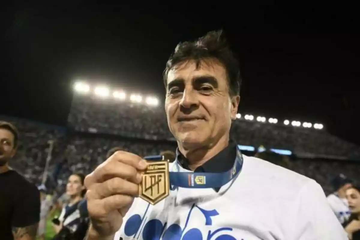 Hombre sonriente mostrando una medalla dorada en un estadio lleno de gente durante la noche Hombre sonriente mostrando una medalla dorada en un estadio lleno de gente durante la noche