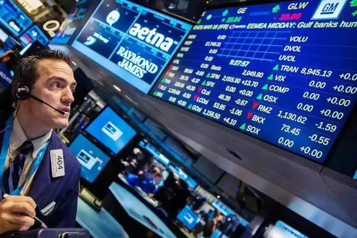 Operador de bolsa con auriculares observando pantallas llenas de información financiera y cotizaciones en una sala de operaciones bursátiles