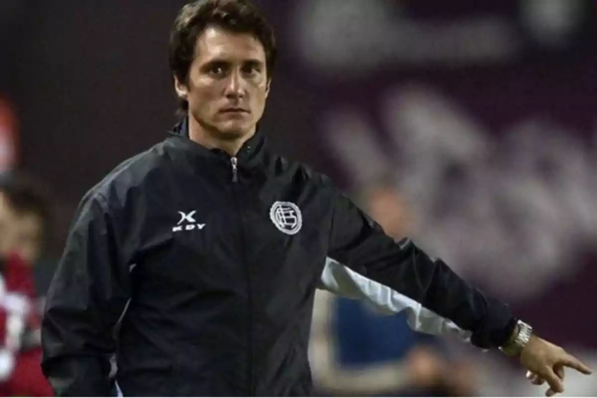 A man in a black sports jacket pointing to the side in a sports setting. A man in a black sports jacket pointing to the side in a sports setting.
