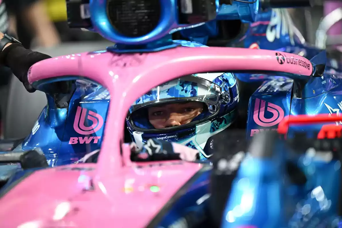Formula 1 driver with a helmet inside a blue and pink single-seater.