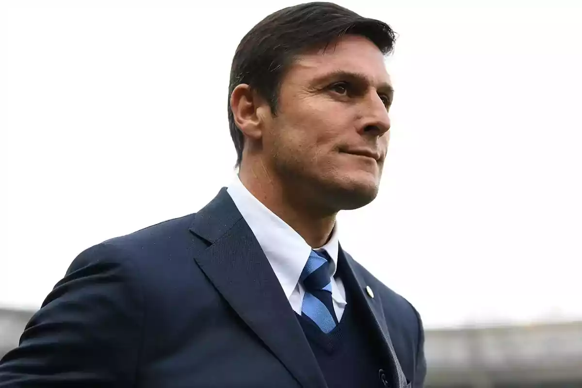 Un hombre con traje oscuro y corbata azul mira hacia el horizonte con expresión seria. Un hombre con traje oscuro y corbata azul mira hacia el horizonte con expresión seria.