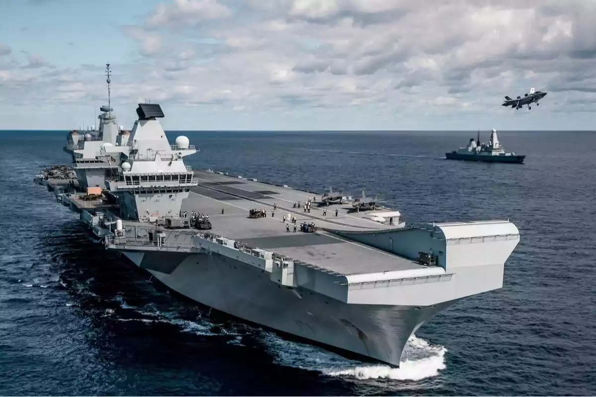 Aircraft carrier sailing at sea with planes on the deck and a plane taking off while a warship accompanies it in the distance Aircraft carrier sailing at sea with planes on the deck and a plane taking off while a warship accompanies it in the distance