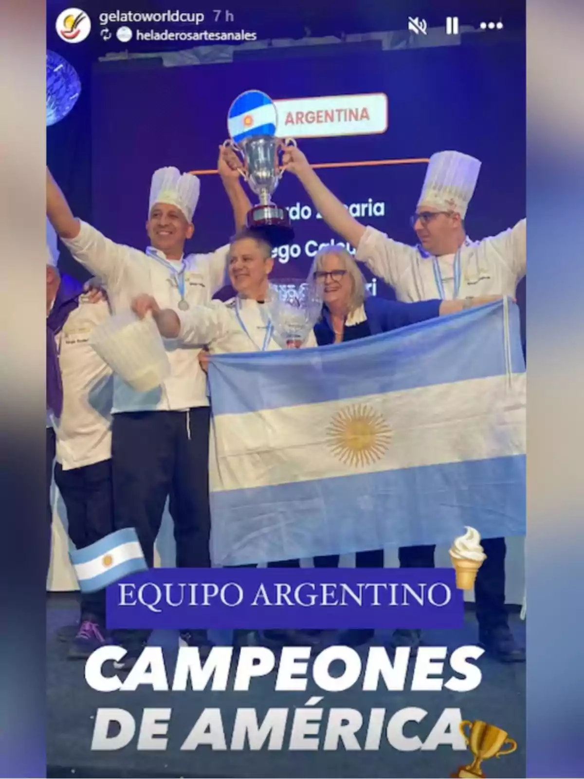 Un grupo de personas con uniformes de chef y gorros sostiene una copa y una bandera de Argentina en un escenario celebrando su victoria como campeones de América en una competencia de helado Un grupo de personas con uniformes de chef y gorros sostiene una copa y una bandera de Argentina en un escenario celebrando su victoria como campeones de América en una competencia de helado