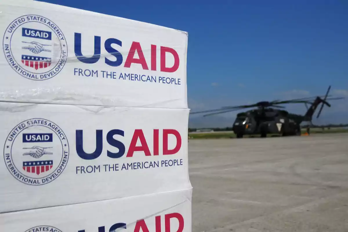 Boxes with the USAID logo at an airport with a military helicopter in the background.