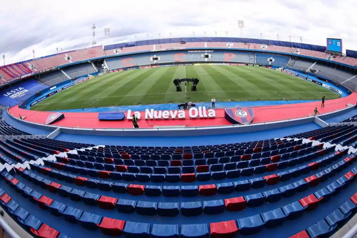 Vista panorámica de un estadio de fútbol vacío con asientos en colores azul y rojo y un campo de juego bien cuidado.