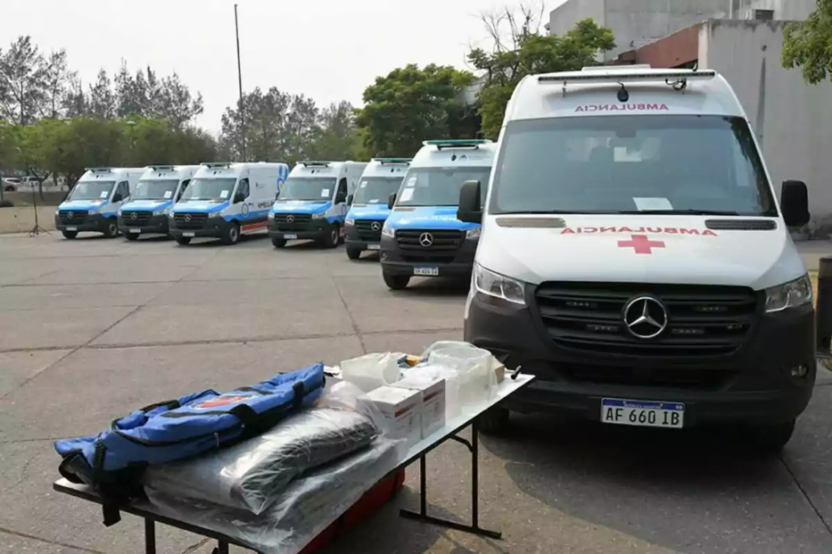 Una fila de ambulancias estacionadas en un área abierta con equipo médico sobre una mesa en primer plano.