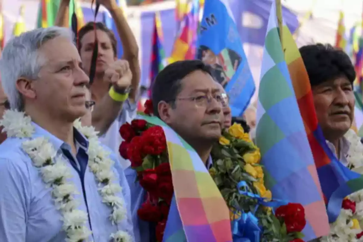 Three men with flower garlands around their necks hold multicolored flags at an outdoor event, surrounded by people and flags in the background. Three men with flower garlands around their necks hold multicolored flags at an outdoor event, surrounded by people and flags in the background.