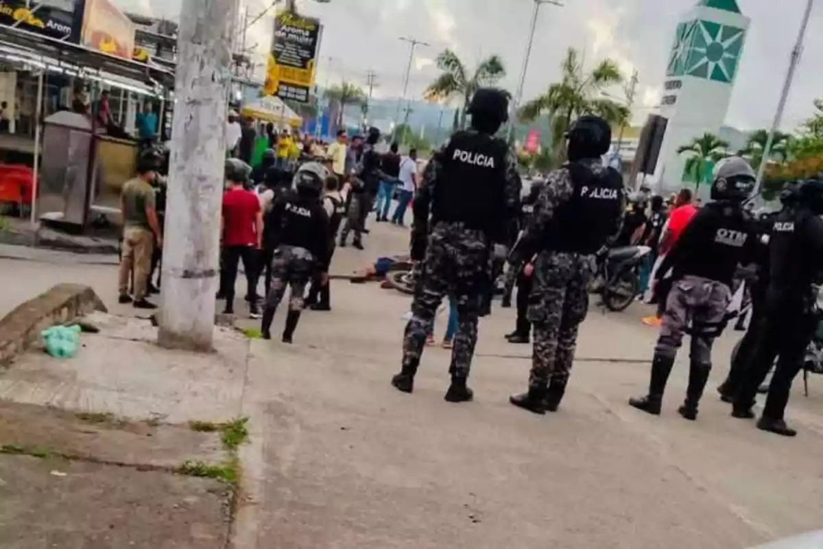 Un grupo de policías con equipo antidisturbios observa una multitud en una calle urbana.