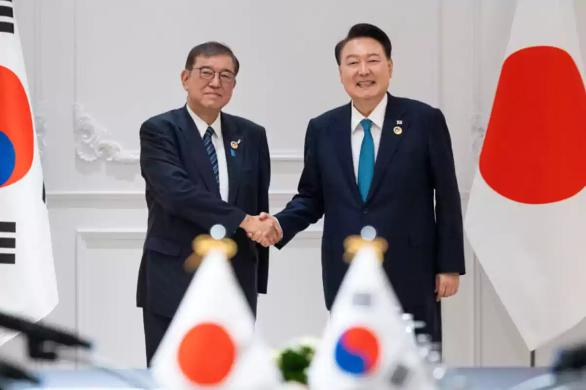 Dos hombres de traje se dan la mano frente a las banderas de Corea del Sur y Japón.