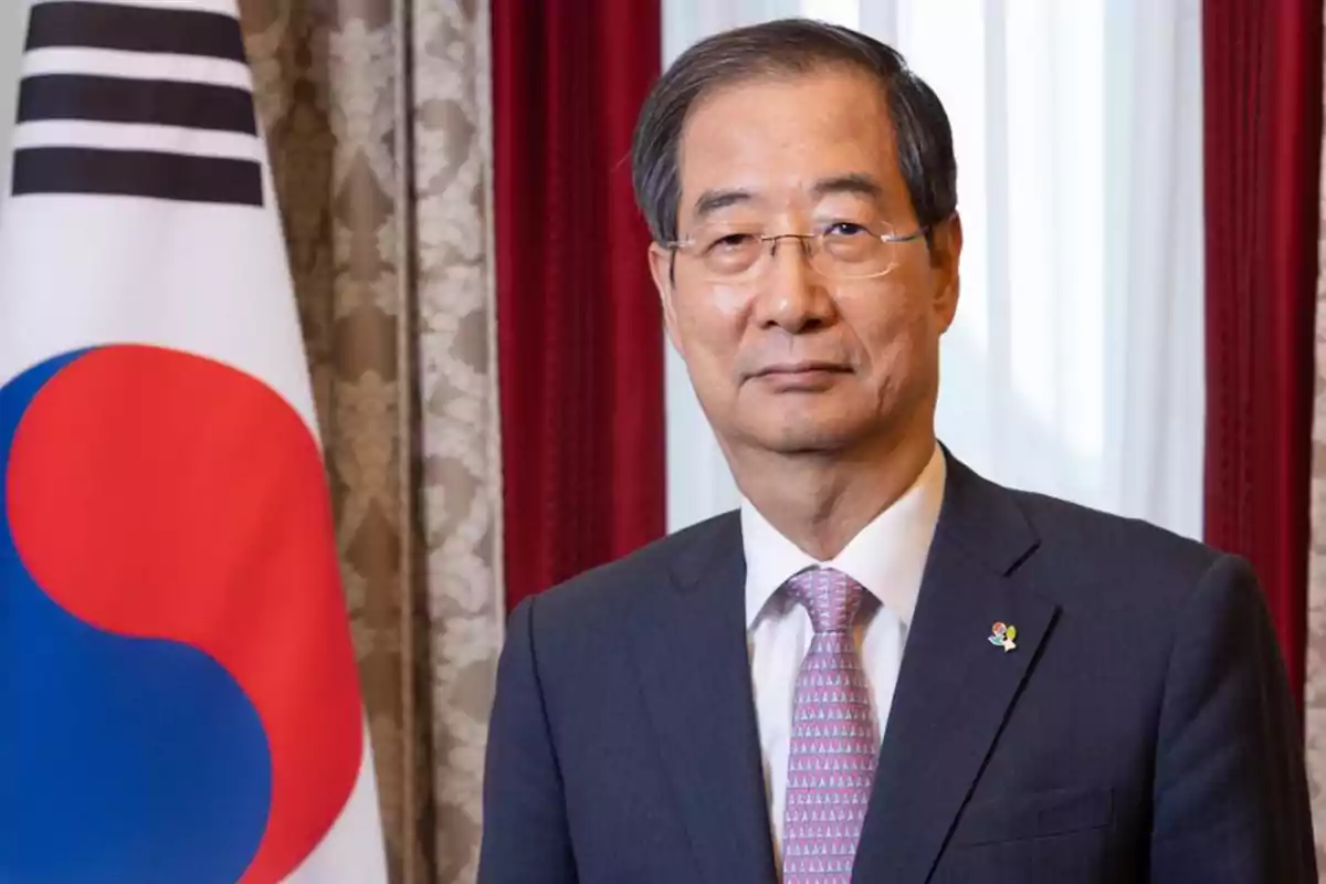 A man in a suit and tie is standing next to a South Korean flag in a formal setting. A man in a suit and tie is standing next to a South Korean flag in a formal setting.