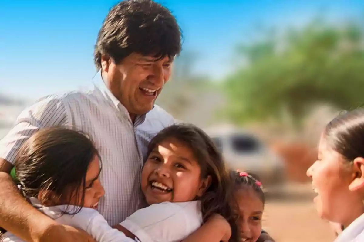 Un hombre sonriente abraza a un grupo de niños felices al aire libre.