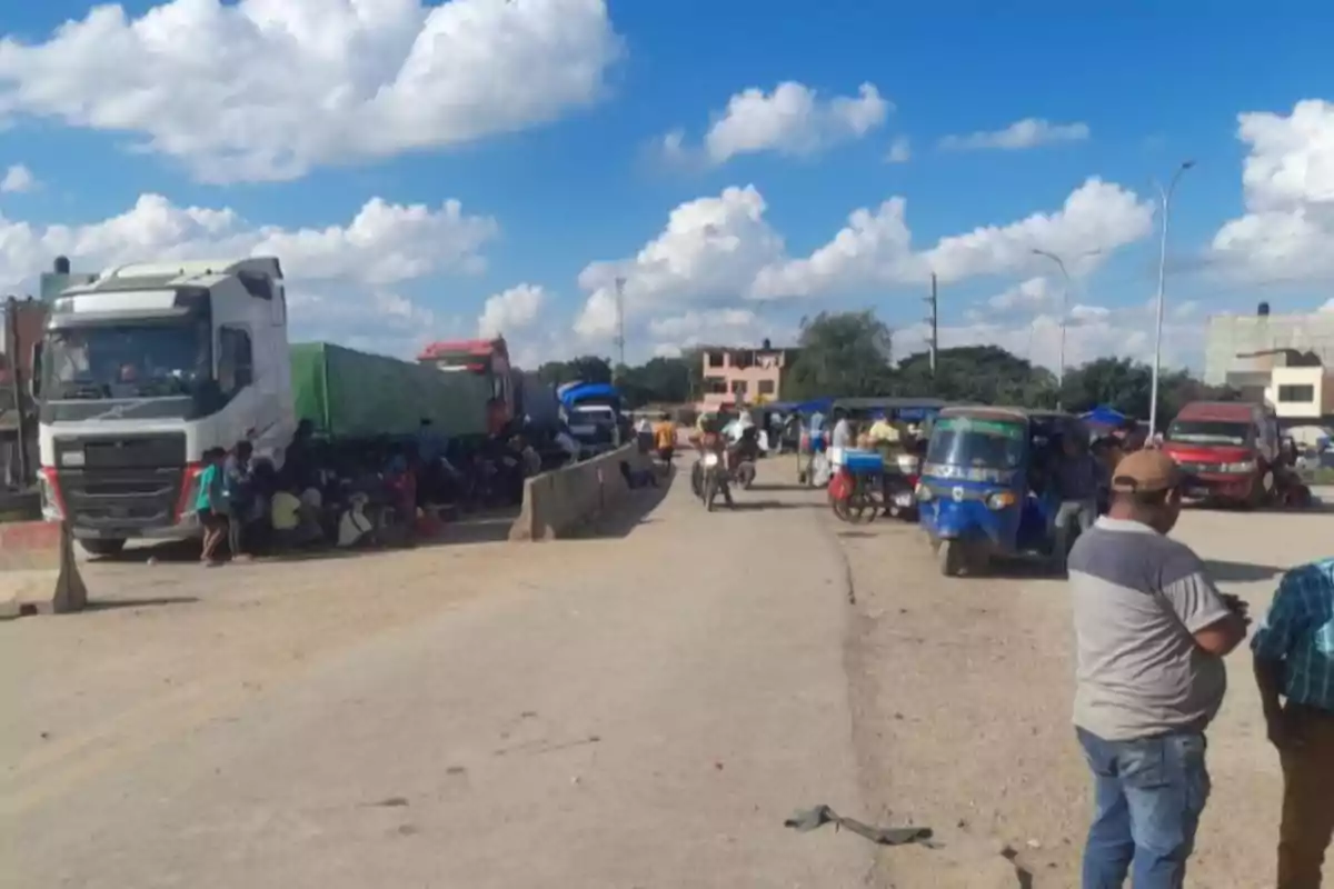 Una carretera con camiones estacionados a un lado y varias personas alrededor en un día soleado. Una carretera con camiones estacionados a un lado y varias personas alrededor en un día soleado.