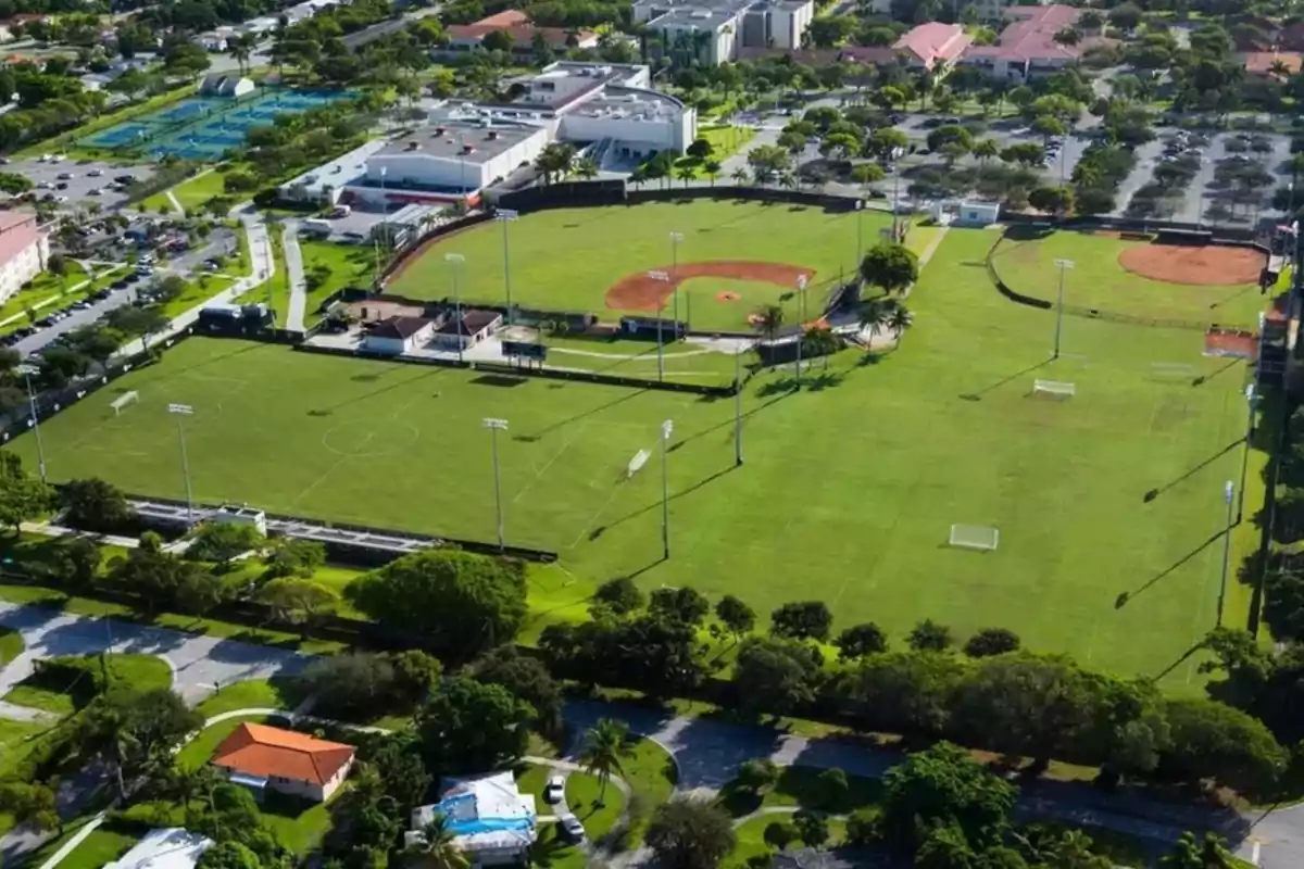 Aerial view of a sports complex with soccer fields, baseball fields, and green areas surrounded by trees and buildings Aerial view of a sports complex with soccer fields, baseball fields, and green areas surrounded by trees and buildings