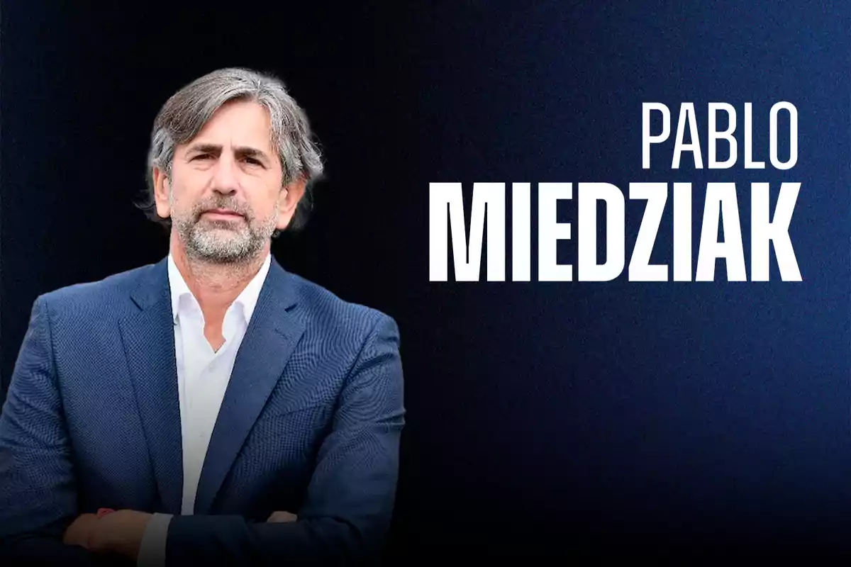 Un hombre de cabello canoso y barba, vestido con un traje azul, aparece junto a un fondo oscuro con texto en letras grandes.